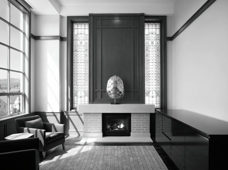 A modern office featuring a fireplace, stained glass windows, an armchair, and a dark cabinet.