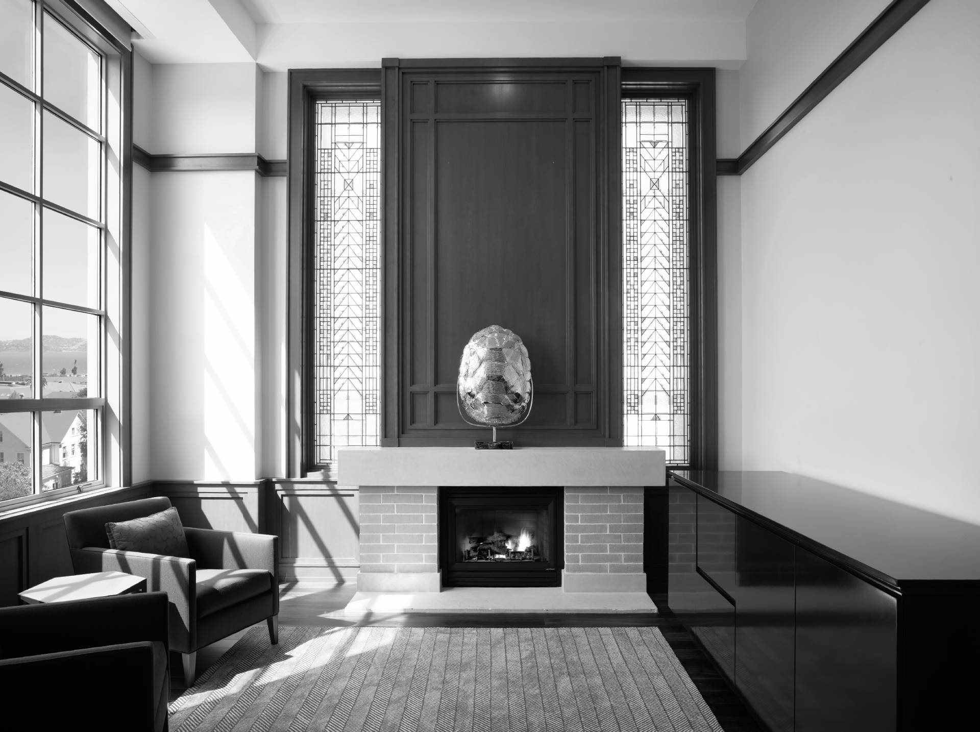 A modern office featuring a fireplace, stained glass windows, an armchair, and a dark cabinet.